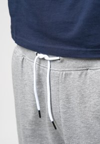 Gros plan sur un pantalon de jogging gris avec un cordon blanc noué en un nœud et un ourlet de chemise bleu marine au-dessus de la ceinture.