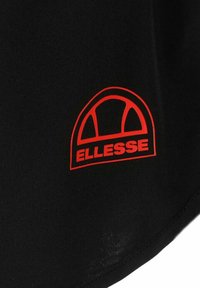 Logo de Ellesse en rojo con diseño semicircular sobre un fondo de tela negra, probablemente parte de ropa o indumentaria deportiva.