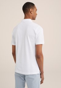 Polo blanco de algodón, con un cuello clásico, mangas cortas y aberturas en los laterales del dobladillo para un ajuste relajado.