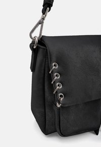 Sac en cuir noir avec rabat, ferrures argentées et œillets décoratifs. Présente une finition texturée et une sangle amovible avec un clip.