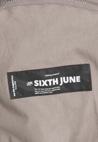 Szara tkanina wewnętrzna z czarną etykietą z białym napisem "SIXTH JUNE" oraz dodatkowymi szczegółami marki. Brak widocznych wzorów lub akcentów.