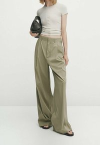 Haut à manches courtes côtelé gris clair associé à un pantalon ample vert olive. Le pantalon a une taille haute, des plis et une texture lisse. Accessoire : sac noir.