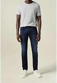 Camiseta gris de cuello redondo combinada con jeans de mezclilla azul oscuro, con corte recto y un sutil desgaste. Se lleva con zapatos blancos tipo slip-on.