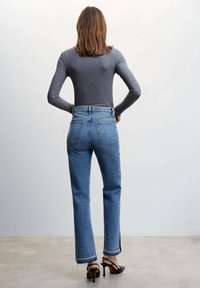 Fitted long-sleeve gray top paired with high-waisted blue denim jeans featuring frayed hems and side slits, worn with black heeled sandals.