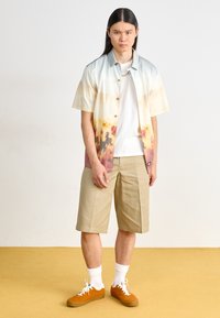 Short-sleeve button-up shirt in gradient pastels with floral prints; paired with beige shorts and orange sneakers. White socks visible.