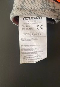 Guanti Reusch World Cup Warrior Neo, grigi e arancioni, realizzati in 85% poliestere e 15% pelle di capra, con fodera in 100% poliestere e etichetta di cura.