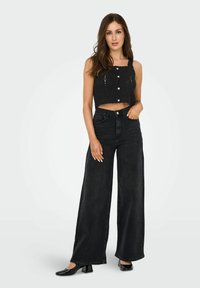 Débardeur noir tricoté court avec des boutons sur le devant, assorti à un jean noir taille haute à jambes larges et des chaussures à talons blocs noires brillantes.