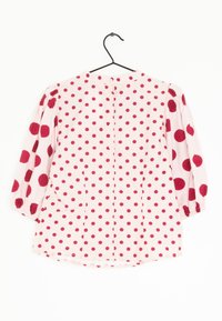 Blusa rosa con grandi pois rossi, maniche lunghe a sbuffo, chiusura con bottoni sul retro e polsini arricciati. Tessuto di cotone liscio.