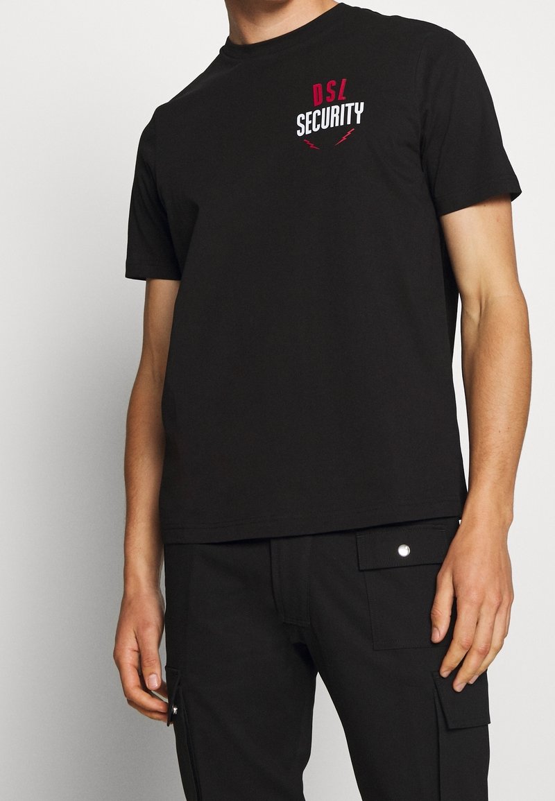 T-shirt noir en coton avec un graphique "DSL SECURITY" rouge et blanc sur la poitrine, col rond et manches courtes.
