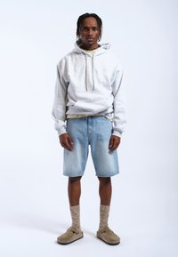 Grijze hoodie met trekkoorden, gedragen over een licht t-shirt. Lichtblauwe denim shorts, gestructureerde bruine sokken en beige instappers.