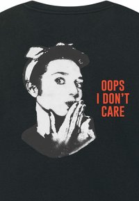 Maglietta nera con una grande grafica di un volto in bianco e nero e testo rosso che recita "OOPS I DON'T CARE." Tessuto morbido, vestibilità standard.