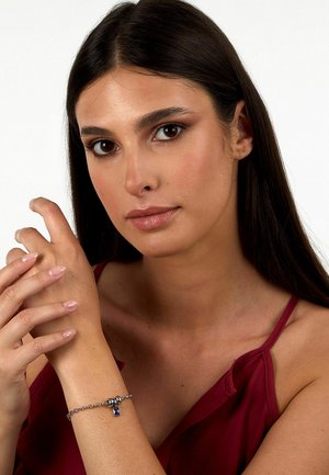 Bracciale in argento con un accento di pietra blu, caratterizzato da un design attorcigliato, indossato su un polso contro uno sfondo neutro.