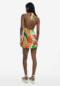 Colorful halter neck dress featuring a deep back, tropical leaf design in orange, green, and blue; smooth fabric with a relaxed fit.
