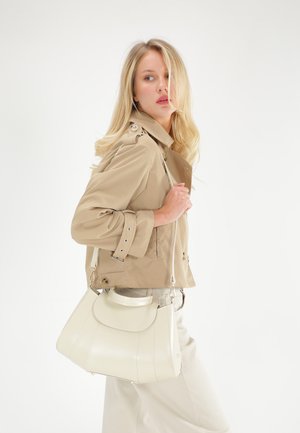 Crème leren handtas met een gebogen vorm en gestikte details, gecombineerd met een beige trenchcoat, voorzien van knopen en ritsaccenten.