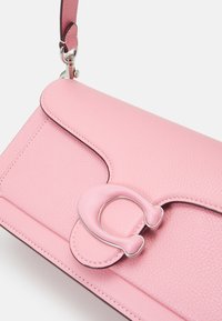 Sac bandoulière en cuir rose avec une surface texturée, une fermeture à rabat et une garniture brillante en métal argenté de forme distinctive.