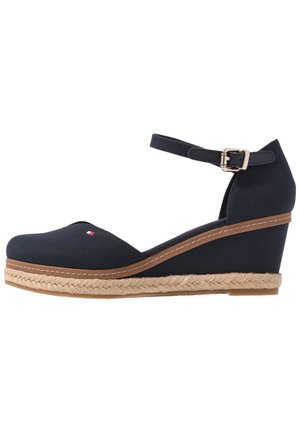 Sandalias cuña en color navy con un upper de tela suave, tira en el tobillo, plataforma envuelta en yute y un sutil acento de logo. Presenta puntera redondeada y detalles de costura.