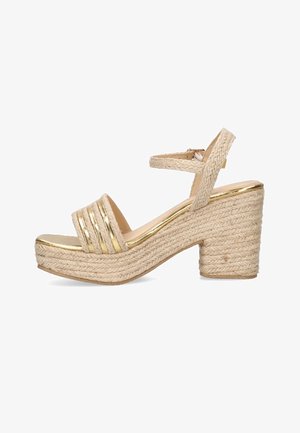 Sandale à plateforme tissée beige avec talon carré, bride à la cheville et accents métalliques dorés sur le bout et la semelle intérieure.