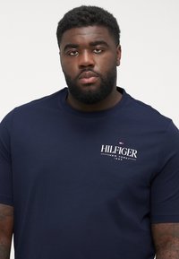 Granatowa koszulka z krótkim rękawem wykonana z mieszanki bawełny, z białym logotypem "HILFIGER" na lewej stronie klatki piersiowej. Klasyczny okrągły dekolt.