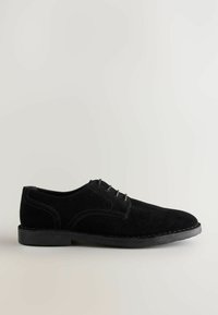 Zapato de hombre de ante negro con perfil bajo, punta redonda, diseño de cordones con cinco ojetes y costuras en contraste en los laterales y la suela.