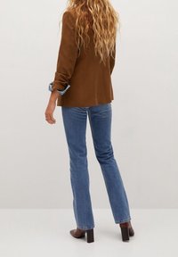 Blazer marron avec des manches retroussées sur un jean en denim bleu clair. Bottines à talons marron. Texture lisse avec une coupe ajustée et un design à jambes droites.