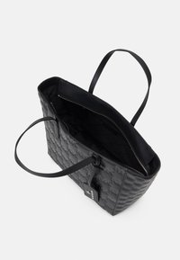 Zwarte totebag gemaakt van textuurmateriaal met sterrenpatroon, twee handvatten en een ritsvak; interieur heeft een quilted ontwerp.