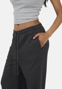 Szary prążkowany top na ramiączkach w połączeniu z ciemnoszarymi spodniami dresowymi z elastycznym pasem i bocznymi kieszeniami. Materiał wydaje się miękki i przewiewny.