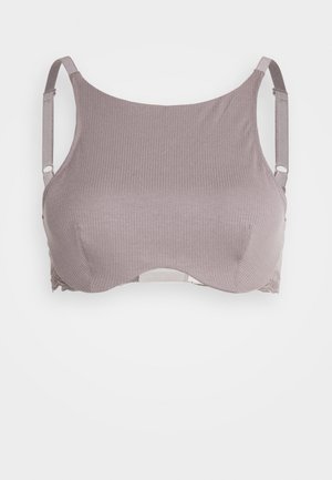 Svetlomalvová podprsenka s rebrovanou textúrou látky, mäkkými košíčkami a nastaviteľnými ramienkami. Má čipkovaný lem pozdĺž základu pre detail.