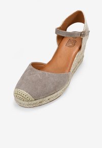 Zapato de cuña beige de espadrille con parte superior de ante, tacón de yute trenzado y correa ajustable en el tobillo. Punta redondeada con detalles de borde texturizados.