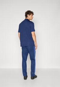 Camisa polo azul-marinho e calças correspondentes com riscas laterais azuis. Feitas de um tecido suave, as calças têm um corte ajustado e assentam acima de sapatos pretos.