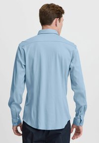 Camisa de manga larga azul claro, hecha de una tela suave, con un cuello tradicional, puños con botón y un dobladillo curved.