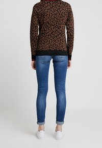 Gebreid vest met een bruin en zwart dierenprint, voorzien van een geribde zoom en manchetten, gecombineerd met blauwe skinny jeans en witte sneakers.