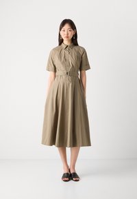 Khaki shirt dress with short sleeves, button front, and a belted waist. Flared skirt with a smooth texture, paired with black slide sandals.
