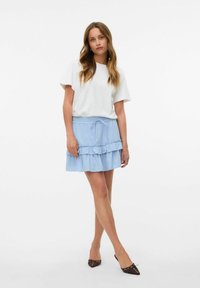 Jupe bleu clair avec un design en volants superposés, dotée d'une taille élastique et d'un cordon de serrage. Assortie à un t-shirt blanc uni et à des chaussures marron.