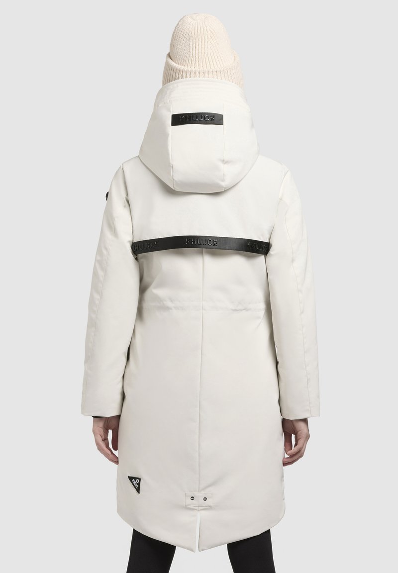 Witte gewatteerde parka met een capuchon, zwarte logostosser over de achterkant en een driehoekige logo patch aan de onderkant. Heeft lange mouwen en een rits.
