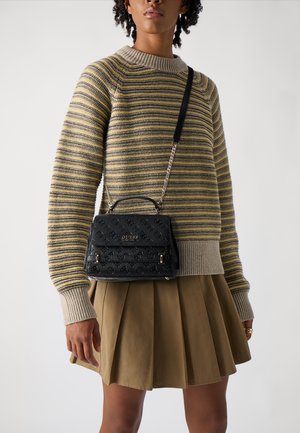 Borsa nera texturizzata con motivi in rilievo, dotata di manico superiore e tracolla a catena, abbinata a un maglione a righe e a una gonna plissettata.
