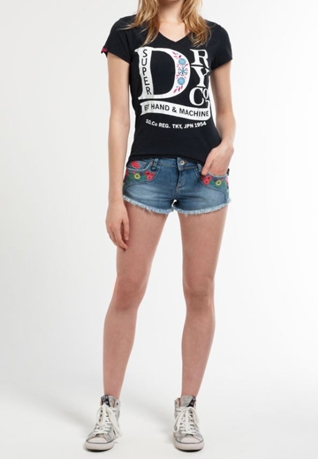 Černé bavlněné tričko s bílým grafickým potiskem, doplněné modrými džínovými šortkami s květinovou výšivkou na předních kapsách. Bílé vysoké tenisky.