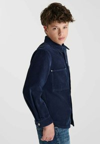 Marineblauwe korduroy shirt met knoopsluiting aan de voorkant, twee borstzakken en lange mouwen. Beschikt over een gestructureerde stof en een klassieke kraagontwerp.