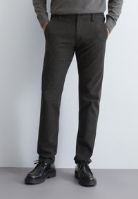 Donkergrijze twillbroek met een rechte pasvorm, voorzien van zijzakken, een knoopsluiting en een gestructureerd patroon. Gecombineerd met zwarte schoenen.