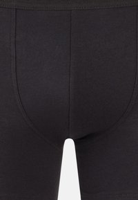 Boxer shorts in cotone nero che mettono in evidenza una texture liscia, un design aderente e una cintura elastica in contrasto con dettagli cuciti sottili.