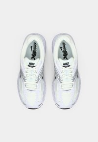 Ζευγάρι λευκών και ασημένιων Nike Air Max Moto 2K sneakers παρουσιασμένο από πάνω σε απλό φωτεινό φόντο.