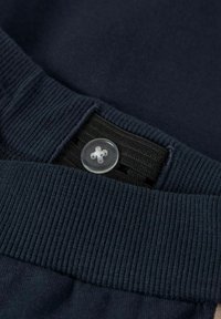 Navy blue garment with a textured waistband featuring a clear plastic button, showing intricate stitching along the edge.