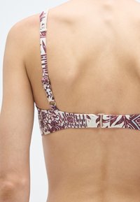 Σουτιέν με υφασμάτινη μοτίβο σε αποχρώσεις βουργουνδί και κρέμ. Ρυθμιζόμενοι ιμάντες και μεταλλικό κλείσιμο με γάντζο στο πίσω μέρος.