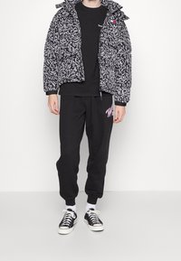Doudoune avec un motif abstrait noir et blanc, associée à un sweat noir et un pantalon de jogging noir. Chaussures noires avec des semelles blanches.