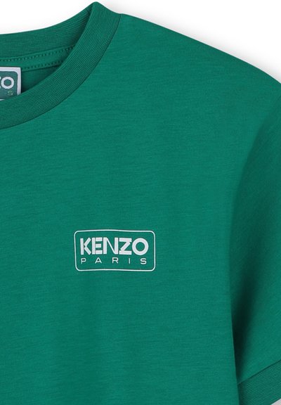 T-shirt en coton vert avec un col rond, arborant un logo rectangulaire blanc inscrit "KENZO PARIS" au niveau de la poitrine. Texture lisse.