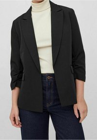 Černý blejzr s upraveným střihem, zapínání na jeden knoflík a s ohrnutými rukávy. Nosit přes smetanový rolák a v kombinaci s džíny s vysokým pasem.