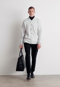 Svetlo šedý pletený cardigan s predným zapínaním na gombíky, v kombinácii s čiernymi nohavicami a čiernou taškou na rameno. Model má pod ním na sebe čierny rolák.