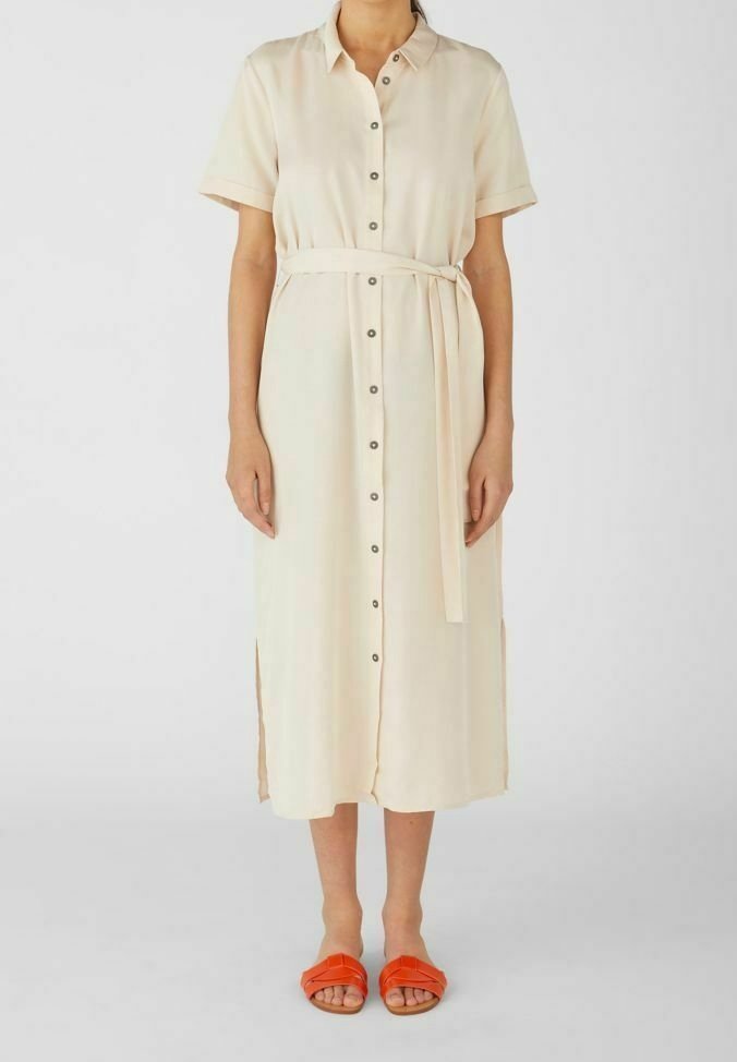 Femme portant une robe midi crème à manches courtes boutonnée, avec ceinture à la taille et sandales ouvertes orange vif.