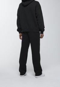 Sudadera con capucha negra de corte holgado y mangas amplias, combinada con pantalones deportivos negros a juego. Textura de tela suave, diseño minimalista.