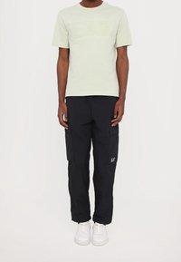 Světle zelené tričko s krátkým rukávem s vyraženým logem "EA7", doplněné černými cargo kalhotami s bočními kapsami a bílými teniskami.