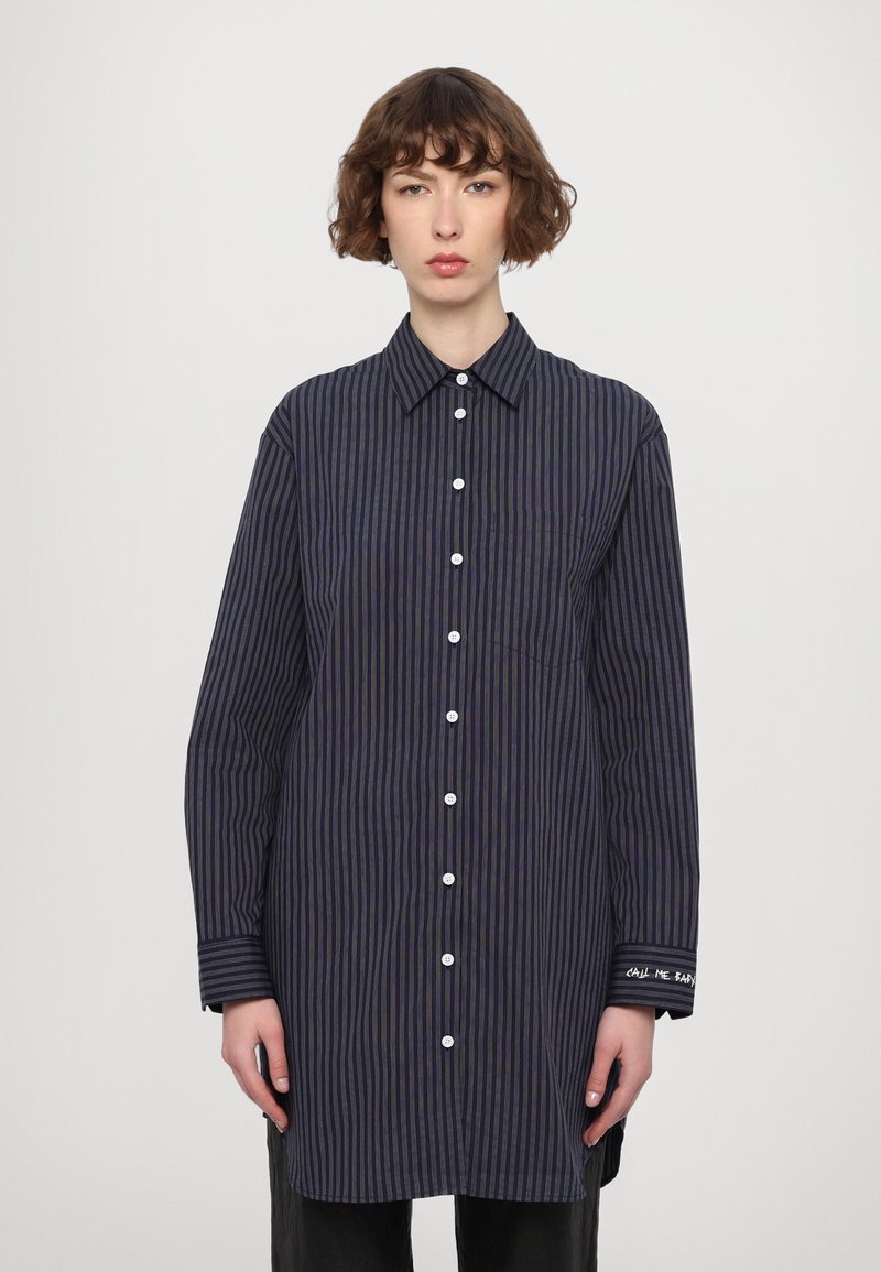 Camisa de botones en azul marino con rayas verticales, que presenta un cuello, mangas largas, un bolsillo en el pecho y un detalle bordado en el puño.